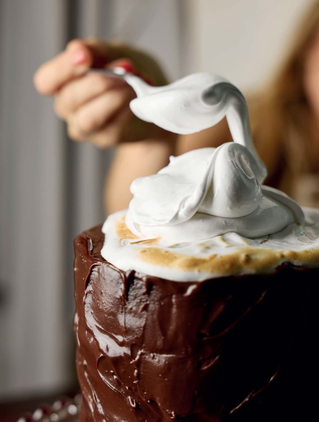 Mano sirviendo merengue sobre pastel de chocolate, fotografía editorial de Mónica Varas Sáenz.