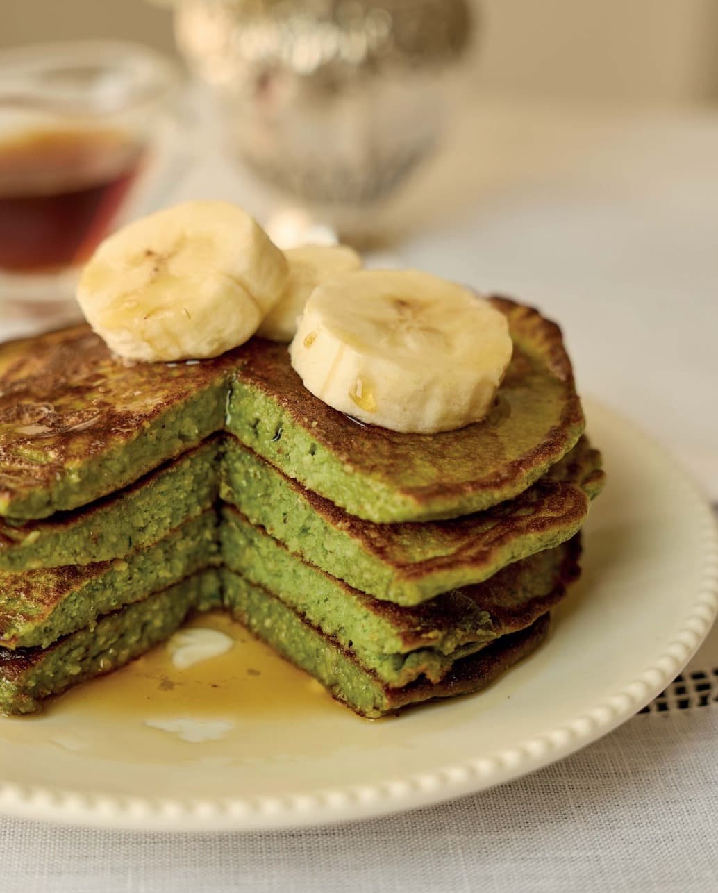 Pila de hot cakes verdes con plátano y café de olla servidos en plato blanco.